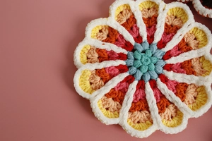 Close-up of hand-crocheted floral coaster with vibrant yarn textures on pink background