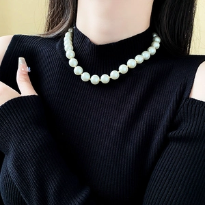Close-up of elegant white pearl necklace on model neck with black knit sweater detail