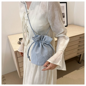 Detailed view of light blue satin drawstring bucket bag with pleated texture and thin strap