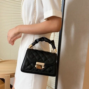 Detail of black quilted crossbody bag featuring gold chain strap and ruffled top handle