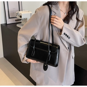 Close-up of black glossy patent leather shoulder bag with chic heart charm and strap