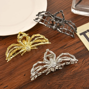 Three metallic spider hair claws in gold, silver, and black on a wood surface