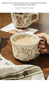 Detailed view of hand-painted ceramic mug with embossed plant motifs on a rustic table