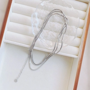 Detail of silver triple-layered snake chain necklace with round charm and extender