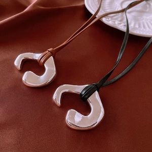Close-up of irregular silver pendants with black and brown leather cords on silk fabric