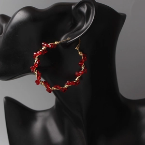 Detailed close-up of large golden hoop earrings decorated with red crystal beads