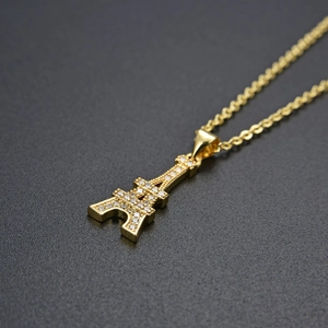 Golden Eiffel Tower pendant necklace with white CZ inlay on dark textured background