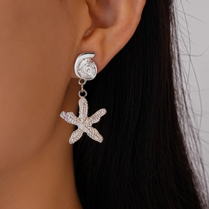 Close-up of asymmetric silver shell and starfish drop earrings worn on a model