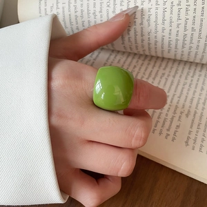 Macro shot of a bright green oval resin ring worn by a model over an open book