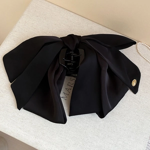 Detail of a black fabric bow hair claw clip with a gold metal tag on a textured surface