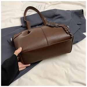 Brown pleated leather tote bag detail with decorative charm and hand-held demonstration