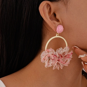 Detail of pink fabric flower earrings with golden rings on model for a spring look