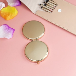 Close-up of a round golden folding pocket mirror on pink background with makeup accessories