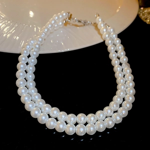 Gros plan d'un collier de perles blanches à deux rangs avec fermoir en argent sur fond noir