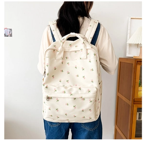 Close-up of beige canvas backpack with pink floral pattern worn by a person