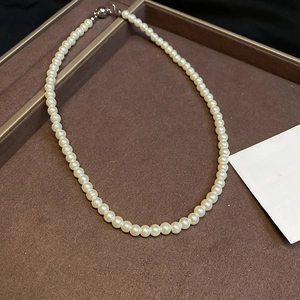 Close-up of elegant white pearl necklace with silver spherical clasp on brown tray