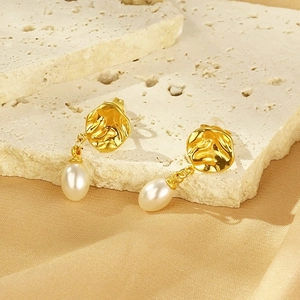 Détail de boucles d'oreilles dorées irrégulières avec pendentifs en perles blanches