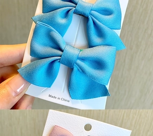 Close-up of a pair of bright blue ribbed ribbon bow hair clips on a display card