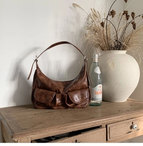 Close-up of brown vintage baguette bag with front flap pockets on a rustic wooden cabinet