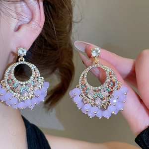 Macro shot of gold circle earrings featuring purple beads and sparkling crystal tassels