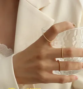 Three-piece set of golden beaded stacking rings shown on fingers holding a glass