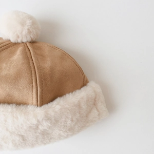 Detail of warm brown faux suede baby beanie with plush white faux fur lining and pompom