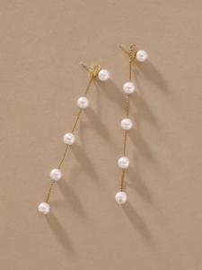 Detailed view of long gold tassel earrings with five white faux pearls on beige background