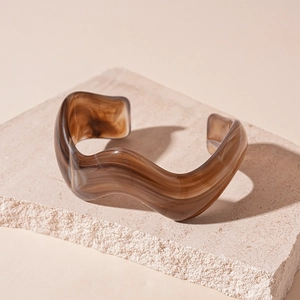 Detailed view of amber acrylic irregular wavy bangle on a textured stone display