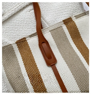 Close-up of striped canvas tote bag showing brown leather handle and fine stitching detail