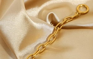 Detailed close-up of golden paperclip chain bracelet with OT toggle clasp on champagne silk