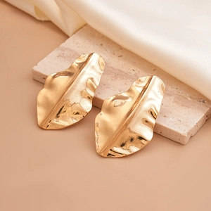Detail of gold metal earrings in leaf shape with hammered texture on marble