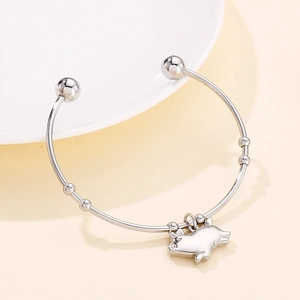 Gros plan d'un pendentif cochon argenté sur un bracelet jonc ouvert à perles rondes