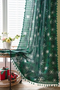 Close-up of green Christmas curtains with white snowflake patterns and tassel edges
