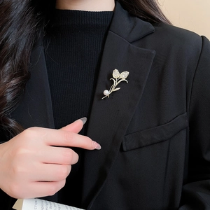Close-up of a 14K gold-plated tulip brooch with zircon and pearl on a black blazer