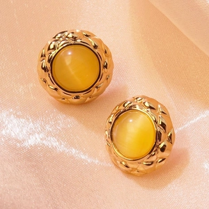 Macro shot of gold button earring with yellow cat eye stone on pink silk background