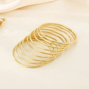 Macro view of nine minimalist 3mm gold stainless steel stackable bangles on a textured surface