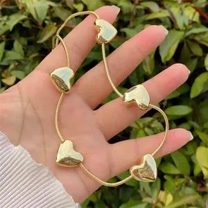 Polished gold heart charm necklace with five pendants shown on neck in sunlight
