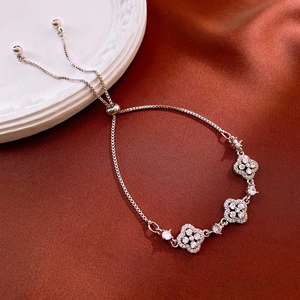 Detail of adjustable silver clover bracelet with white zircons on red silk background