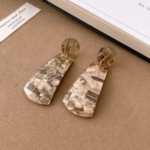 Detailed macro shot of grey and beige mosaic resin geometric earrings on a brown surface