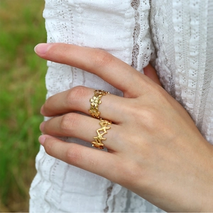 Detail of gold starfish and flower rings worn on hand with a green lawn background