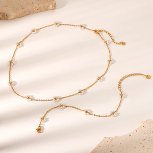 Dettaglio collana a catena dorata con margherite di perle su superficie di pietra