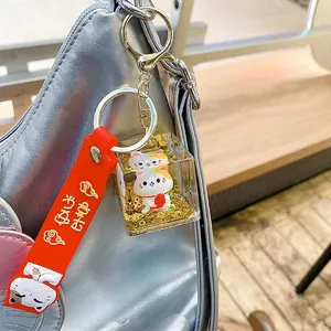 Lucky Cat acrylic keychain with golden flowing sand and red strap on a silver bag