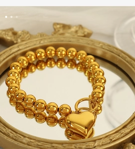 Detailed shot of golden beaded bracelet with heart pendant on a decorative mirror tray