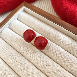 Macro detail of red enamel square stud earrings resting on a beige velvet jewelry box