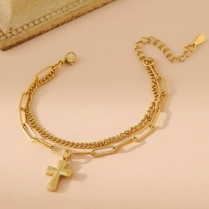 Bracelet double couche en acier inoxydable doré avec pendentif croix sur fond beige uni