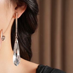 Close-up of long silver teardrop earrings with faceted clear crystals on a model