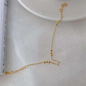 Detail view of gold beaded bracelet with O-link chain, lobster clasp and heart pendant