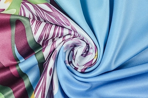 Close-up of floral print fabric with purple flowers and green leaves on royal blue silk