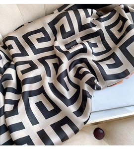 Detail view of beige silk scarf with black Greek key patterns on a minimalist tray