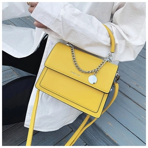 Detail of yellow flap handbag with silver chain strap and metal pendant on white shirt